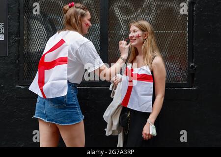London (UK), 11. Juli 2021: Zwei Fußballfans der englischen Euro 2020 malen sich die Gesichter der anderen an, bevor sie sich die englischen Verse ansehen Stockfoto