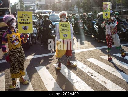 South Jakarta, Indonesien. Juli 2021. Mitglieder der Aku Badut Indonesian Community (ABI) in Clownkostümen zeigen Plakate, die das Tragen von Gesichtsmasken als Vorsichtsmaßnahme gegen die Verbreitung von Covid19 unterstützen. Mitglieder der Aku Badut Indonesia Community (ABI) gingen auf die Straße in Jakarta, um sich für die Umsetzung von Gesundheitsprotokollen während der Covid-19-Pandemie zu einsetzen. Kredit: SOPA Images Limited/Alamy Live Nachrichten Stockfoto