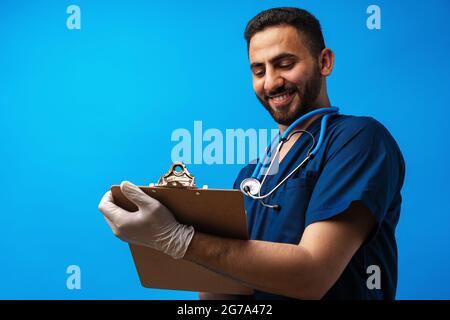 Junger arabischer Arzt mit einer Zwischenablage auf blauem Hintergrund Stockfoto
