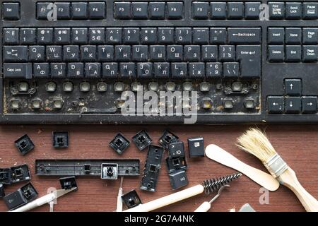 Alte, schmutzige Computertastatur mit entfernten Tasten. Die Werkzeuge für Reparatur und Reinigung auf dem Tisch im Werkstattarbeitsplatz. Nahaufnahme Stockfoto