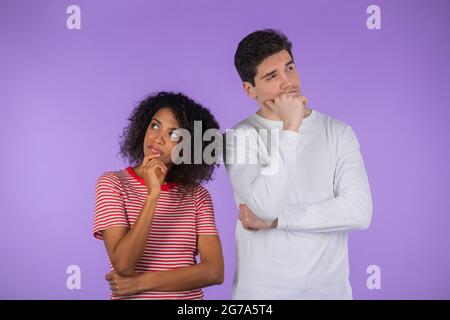 Interracial denken erwägen Paar auf lila Studio-Hintergrund. Mann und Frau schauen in verschiedene Richtungen und jeder denkt über sein Problem nach Stockfoto