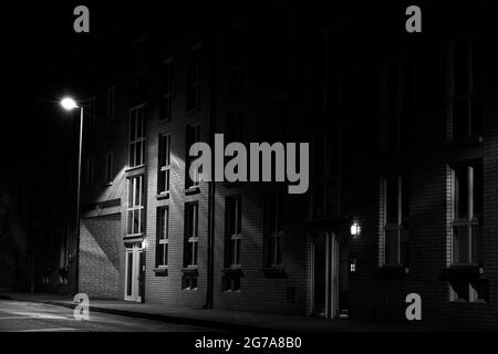 Nachts auf der Straße wird das Apartmentgebäude von einer Straßenlaterne beleuchtet, ohne Menschen, schwarz-weiß, Low Key Photography Stockfoto