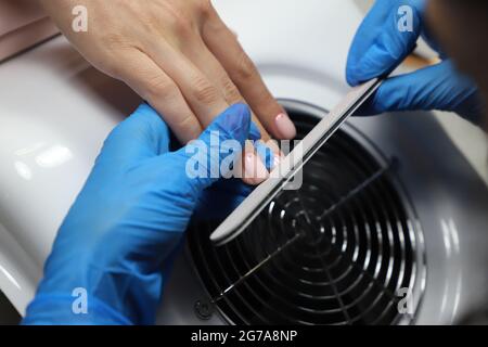 Nahaufnahme des Prozesses der Formung von Nägeln mit Nagelfeile an weibliche Kundin im Schönheitssalon. Erfahrene Kosmetikerin in Schutzhandschuhen bei der Maniküre. Stockfoto