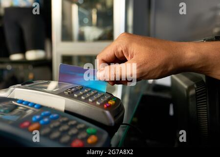 Hand des Kassierers, der die Kreditkarte mit dem POS-Gerät durchzieht, wenn er die Zahlung annimmt Stockfoto