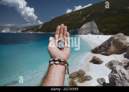 Hand hält einen Kompass auf dem Strand im Hintergrund Stockfoto