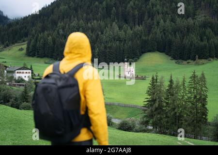 Wandermann mit Rucksack Genießen Sie den Blick auf die St. Johann Kirche im Val di Funes, Dolomiten, Italien, Europa Stockfoto