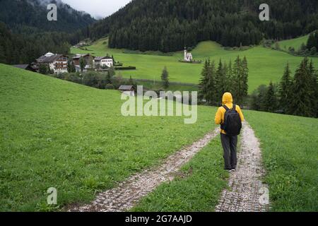 Ein Mann mit Rucksack, der das Val di Funes Tal hinunter zur St. Johann Kirche, Dolomiten, Italien, Europa wandert Stockfoto