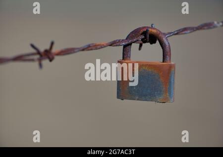 Verrosttes Vorhängeschloss hängt am Stacheldraht, symbolisches Bild der Gefangenschaft, Stuttgart, Baden-Württemberg, Deutschland Stockfoto