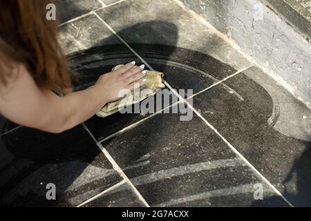 Wischen Sie die Fliesen mit Staub ab. Schmutz von der Oberfläche entfernen. Ein Lappen in der Hand einer Frau. Reinigung von Staub auf einem Stein. Stockfoto