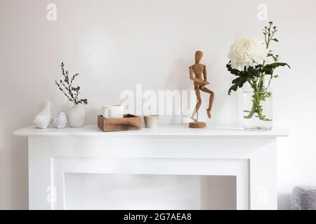 Eine Chrysantheme in transparenter Vase, Korkbrett mit leeren Blättern, ein Holztablett mit Tasse Kaffee, Vase mit Eukalyptus, ein Spiegel und eine Figur von Stockfoto