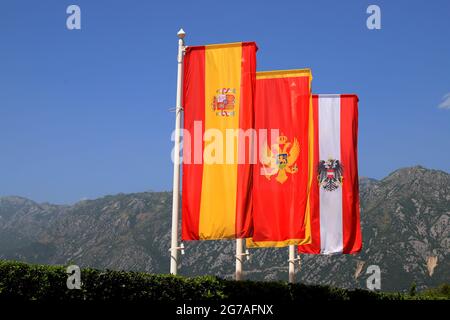 Flaggen mit den Wappen von Montenegro, Österreich, Spanien fliegen vor dem Hintergrund der Berge über die Bucht von Kotor. Alte Stadt Pera Stockfoto