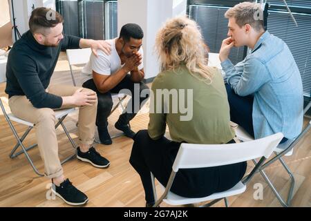 Multiethnische, vielfältige Menschen, die depressive afroamerikanische junge Männer während der Gruppentherapie unterstützen. Stockfoto
