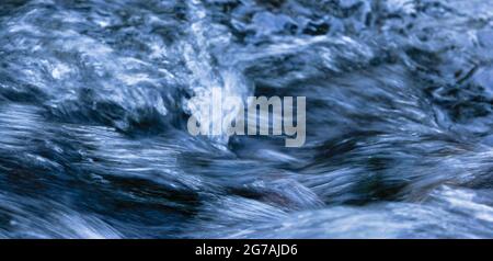 Aufgewühltes Wasser mit Schaumstoffkopf und Spray in weiß, hellblau, dunkelblau und schwarz als Panorama Stockfoto