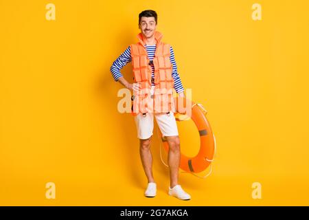 Ganzkörper-Foto von jungen glücklichen Mann halten Rettungsschwimmer Kreis tragen Weste isoliert auf gelbem Hintergrund Stockfoto