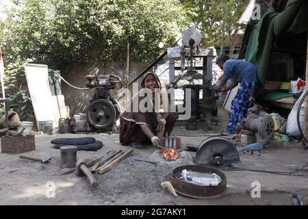 Indische Familie beschäftigt sich mit handwerklicher Schmiede. Eine Frau hält ein glühend heißes Metall in der Schmiede. Die Familie lebt in einem Zelt. Stockfoto