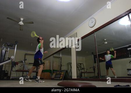 Ein junger Badmintonathlet übt verschiedene Schläge und Schritte vor einem großen Spiegel im Jaya Raya Badmintonclub in Jakarta, Indonesien. Stockfoto