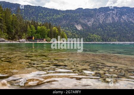 Blick über das türkisfarbene Wasser des Eibsees auf Wälder und Hütten am See, Grainau, Oberbayern, Deutschland Stockfoto