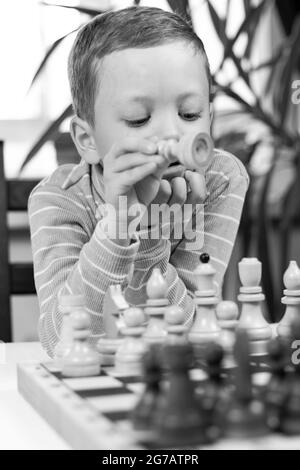 Netter siebenjähriger Junge, der zu Hause auf einem weißen Holztisch Schach spielt. Selektiver Fokus. Nahaufnahme. Hochformat Stockfoto