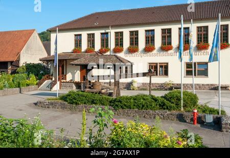 Deutschland, Baden-Württemberg, Vogtsburg im Kaiserstuhl-Achkarren, Gebäude der Weingenossenschaft Achkarren, davor eine historische Weinpresse mit einem schwindelerregenden Baum, in der Kaiserstuhl-Kulturlandschaft. Stockfoto