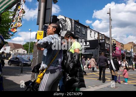Junge schwarze Frauen, die auf dem Straßenmarkt einkaufen, und Menschen, die im Sommer die Straße überqueren, auf der Walthamstow High Street London E17 UK KATHY DEWITT Stockfoto