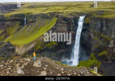 Luftaufnahme des Menschen, der auf der Klippe steht und das Island Highland Valley und den Haifoss Wasserfall genießt Stockfoto