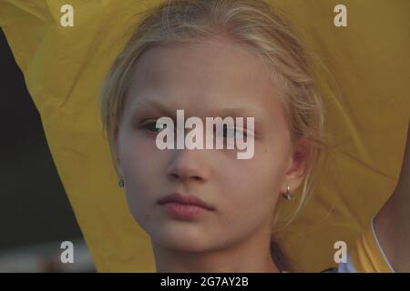Porträt eines blonden Teenagers im Gesicht im Freien auf gelbem Hintergrund. Das blonde Mädchen sieht nachdenklich beiseite. Stockfoto