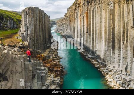 Wanderer in roter Jacke besuchen den Basaltschlucht von Studlagil mit seltenen vulkanischen Basaltsäulenformationen in Island. Stockfoto
