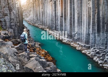 Wanderfrau mit Rucksack genießt den Studlagil Canyon. Einzigartige Jokulsa Basaltkolen und EIN Brufluss. Spektakuläre Outdoor-Szene von Island, Europa. Schönheit der Natur Konzept Hintergrund. Stockfoto