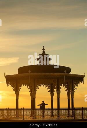 Brighton Bandstand bei Sonnenuntergang. Brighton, East Sussex, England. Silhouette einer Person mit ausgestreckten Armen. Stockfoto