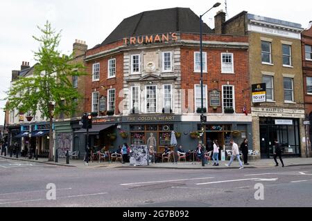 Menschen, die an Tischen sitzen, die sich außerhalb des Golden Heart Pubs an der Ecke Commercial St & Hanbury Street East London E1 KATHY DEWITT befinden Stockfoto