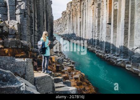 Wanderfrau mit Rucksack genießt den Studlagil Canyon. Einzigartige Jokulsa Basaltkolen und EIN Brufluss. Spektakuläre Outdoor-Szene von Island, Europa. Schönheit der Natur Konzept Hintergrund. Stockfoto