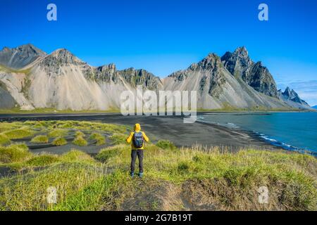 Mann Wanderer mit Rucksack an schwarzen Sanddünen auf der Stokksnes Landzunge an der südöstlichen isländischen Küste mit Vestrahorn. Farbenfroher Sommermorgen Island, Europa. Stockfoto