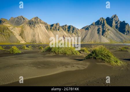 Island. Luftaufnahme einer Wanderin mit Rucksack an schwarzen Sanddünen auf der Stokksnes-Landzunge an der südöstlichen isländischen Küste mit Vestrahorn. Europa. Stockfoto
