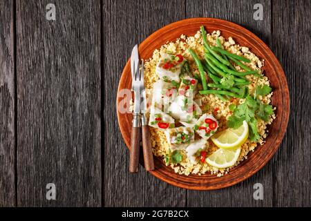 Bacalhau com todos, Kabeljau mit Bulgur, gedämpfte grüne Bohnen, bestreut mit scharfer Chilischote und Frühlingszwiebeln auf einem rustikalen Teller, auf einem Holztisch, por Stockfoto