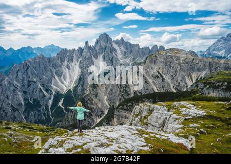 Luftaufnahme einer Wanderin grüner Jacke mit erhobenen Händen, die die Berggipfel der Cadini di Misurina der italienischen Alpen, der Dolomiten, Italiens, Europas bewundert Stockfoto