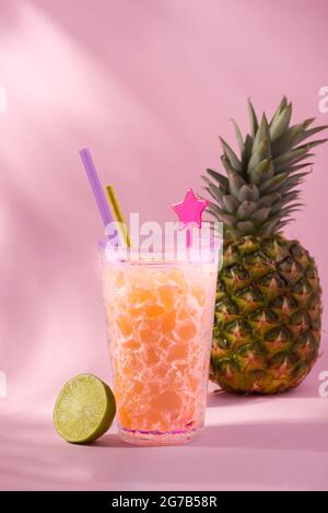 Frischer Ananassaft in einem Cocktailglas gegen Ananasfrüchte und rosa Hintergrund. Hallo, Sommerkonzept. Stockfoto