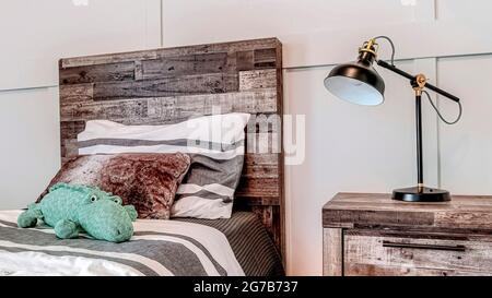 Pano-Lampe auf dem Beistelltisch neben dem Bett mit Holzkopfteil an der getäfelten Wand Stockfoto