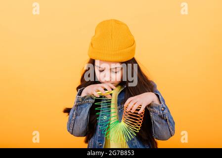 Ein Mädchen in einem mehrfarbigen Hemd hält ein mehrfarbiges, slinky Spielzeug In ihren Händen Stockfoto