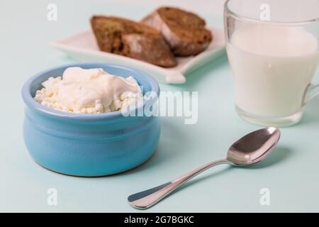 Quark in einer blauen Schüssel mit Sauerrahm und Honig. Geröstetes Brot auf einem Teller. Frühstück am Morgen. Stockfoto