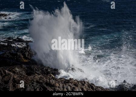 Wellen, die durch ein Loch im Felsen bei Etang Sale passieren Stockfoto