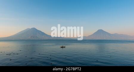 Atitlan Lake Panorama mit maya indigenen Mann in Fischerboot und Vulkan bei Sonnenaufgang, Panajachel, Guatemala. Stockfoto