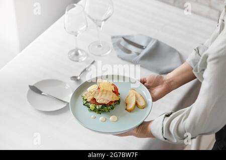 Kellnerin legte Teller mit leckerem Caesar Salat auf den Tisch im Restaurant, Nahaufnahme Stockfoto