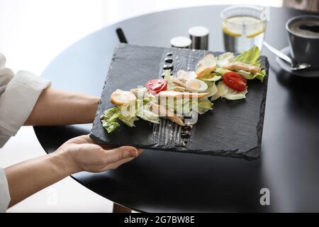 Kellnerin legte Teller mit Caesar Salat auf den Tisch im Restaurant, Nahaufnahme Stockfoto