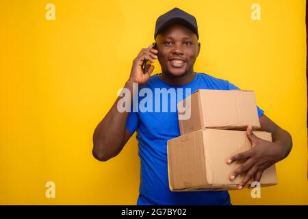 Ein afrikanischer Entsendungsmann, der mit einem Smartphone anruft, Boxen trägt und eine Gesichtskappe trägt Stockfoto