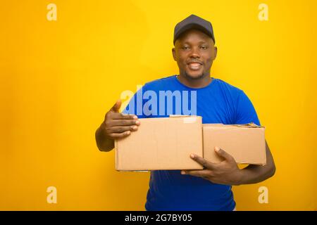 Ein afrikanisches Lieferpersonal oder ein Versandmann, der ein blaues Hemd trägt, Boxen trägt und eine Gesichtskappe trägt Stockfoto