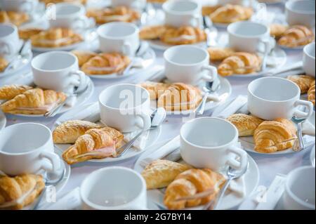 Viele Croissants auf einer Schüssel mit leeren Kaffeetassen auf dem Tisch, die für die Teepause auf einer Geschäftskonferenz serviert werden können Stockfoto