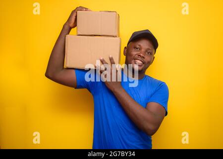 Ein afrikanisches Lieferpersonal oder ein Versandmann, der ein blaues Hemd trägt, Boxen trägt und eine Gesichtskappe trägt Stockfoto