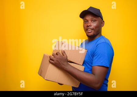 Ein afrikanisches Lieferpersonal oder ein Versandmann, der ein blaues Hemd trägt, Boxen trägt und eine Gesichtskappe trägt Stockfoto