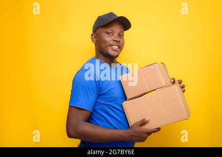 Ein afrikanisches Lieferpersonal oder ein Versandmann, der ein blaues Hemd trägt, Boxen trägt und eine Gesichtskappe trägt Stockfoto