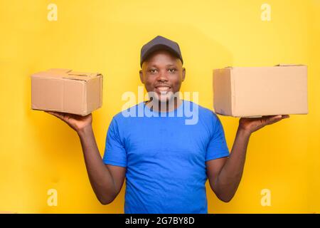 Ein afrikanisches Lieferpersonal oder ein Versandmann, der ein blaues Hemd trägt, Boxen trägt und eine Gesichtskappe trägt Stockfoto